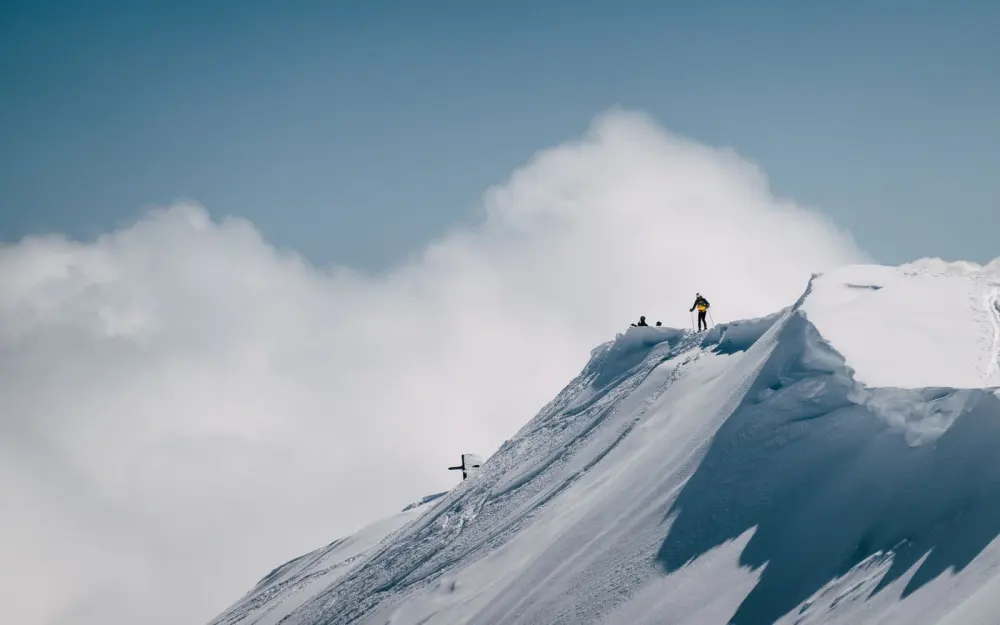 Symbolbild: Mountain climber standing alone on snowy peak with blue sky and clouds.