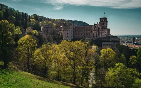 Symbolbild: A scenic view of Heidelberg Castle surrounded by lush spring foliage under a blue sky.
