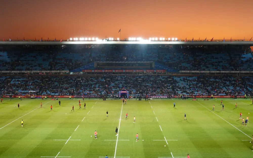 Symbolbild: Exciting rugby game unfolding under stunning sunset in large stadium.
