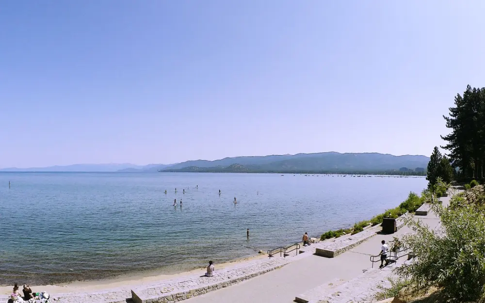 Symbolbild: Serene lakeside scene with distant mountains and clear blue skies.
