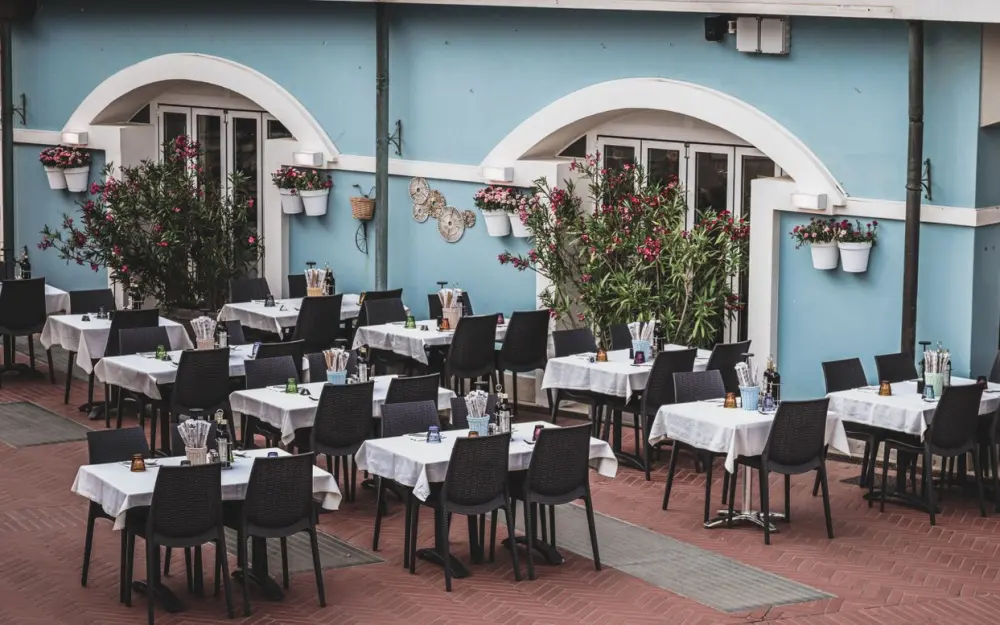 Symbolbild: Cozy outdoor cafe with neatly arranged tables and a vibrant blue facade, perfect for dining.