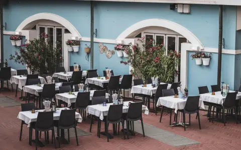 Symbolbild: Cozy outdoor cafe with neatly arranged tables and a vibrant blue facade, perfect for dining.