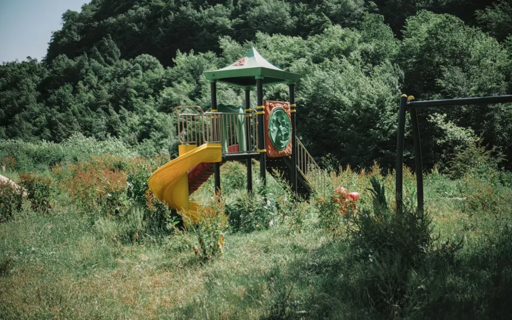 Symbolbild: A colorful playground slide amidst lush greenery in a peaceful countryside environment.
