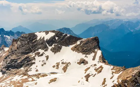 Symbolbild: A breathtaking view of a snow-capped alpine peak under a partly cloudy sky, showcasing rugged mountain beauty.