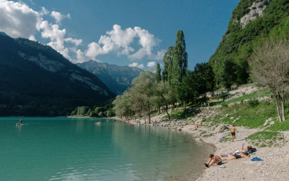 Symbolbild: Sunny day at a scenic Trentino-South Tyrol lake with lush mountains and relaxing beachgoers.
