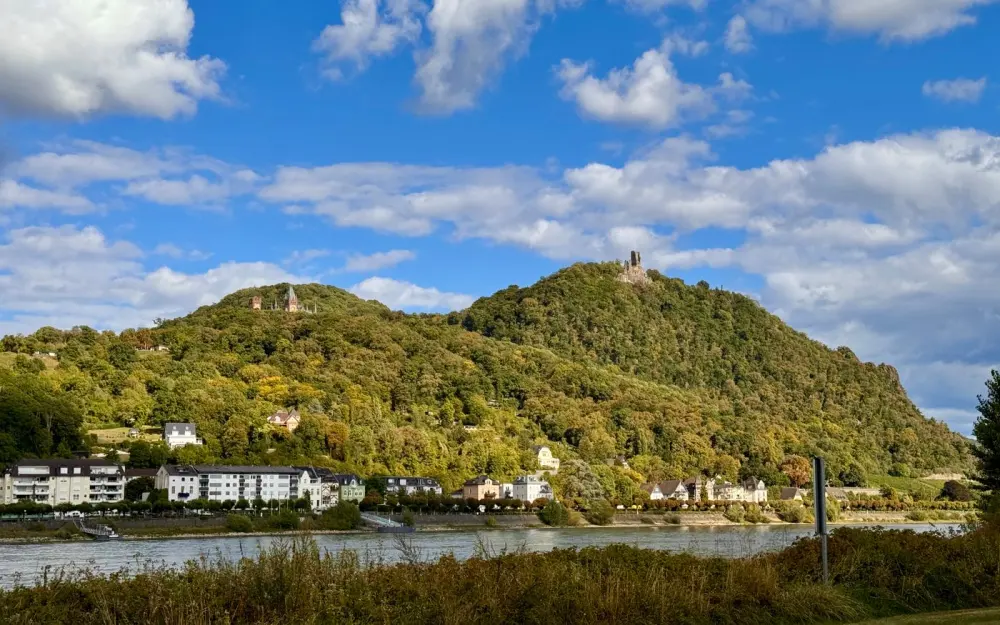 Symbolbild: Idyllic landscape of the Rhine Valley with lush hills, historic ruins, and flowing river under a blue sky.