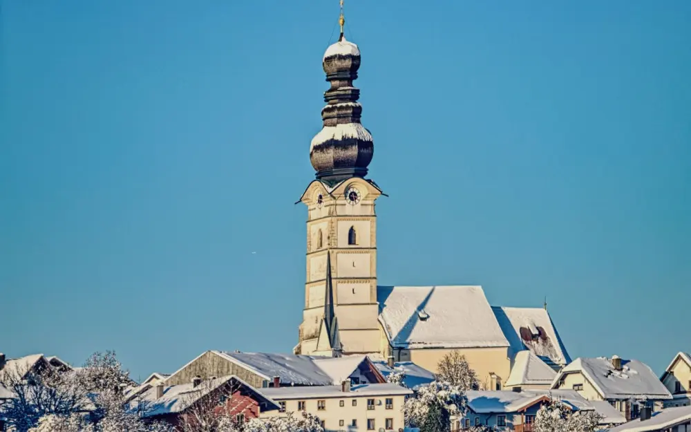 Symbolbild: Snowy winter view of a historic church with an onion dome and scenic blue sky.