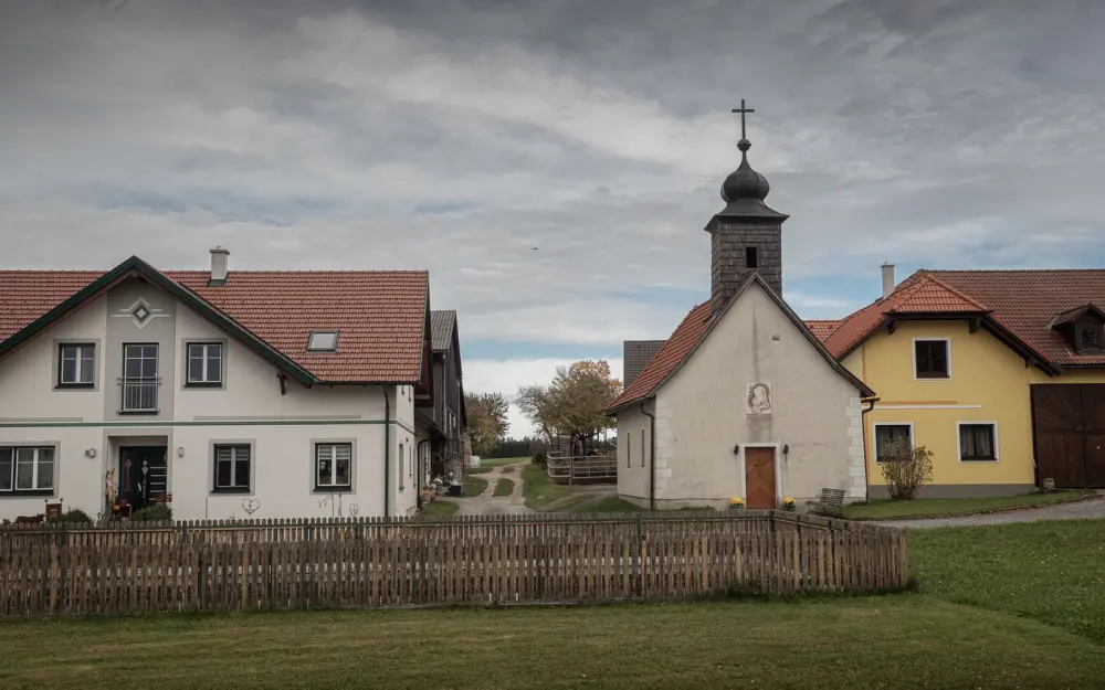 Symbolbild: Charming European village scene featuring houses and a chapel under a cloudy sky.