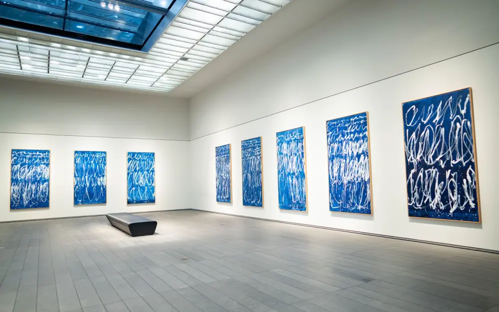Symbolbild: Spacious modern art gallery featuring a collection of blue abstract paintings on display.