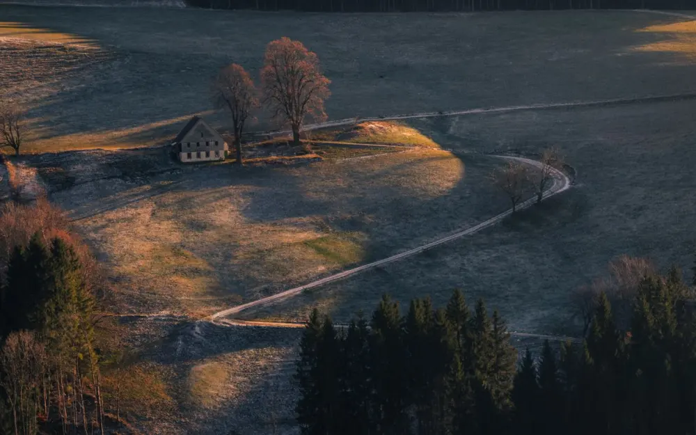 Symbolbild: Aerial view of a lone house on a hill with surrounding landscape at sunrise, creating a serene scene.