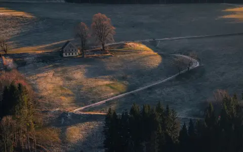 Symbolbild: Aerial view of a lone house on a hill with surrounding landscape at sunrise, creating a serene scene.