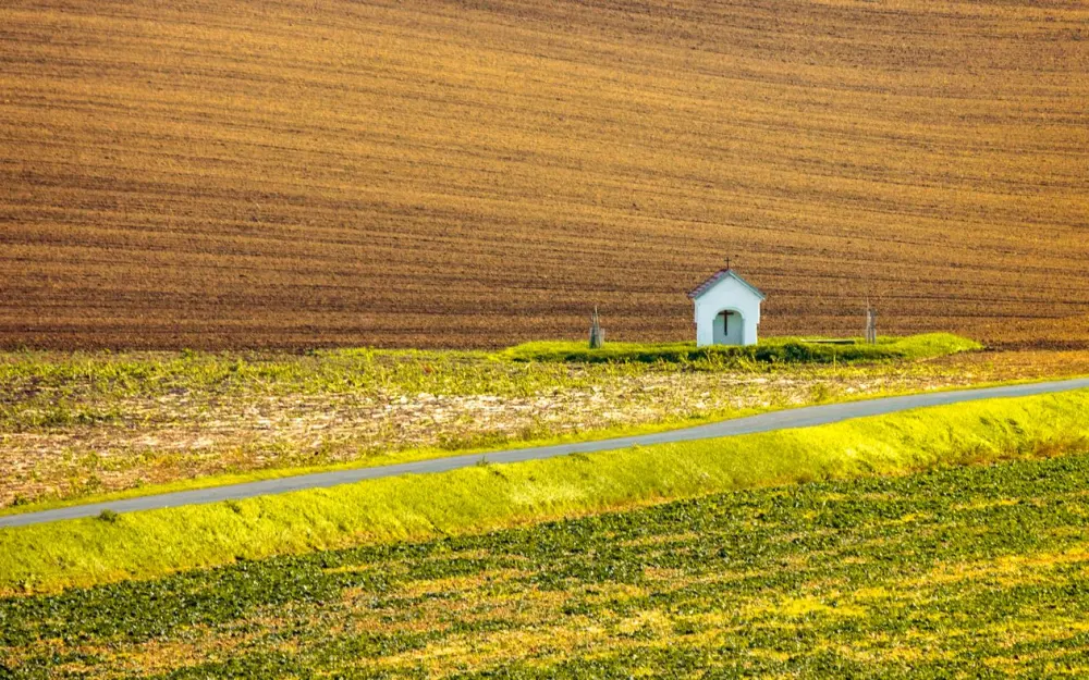 Symbolbild: A serene chapel amidst lush fields in South Moravian Region, Czech Republic.
