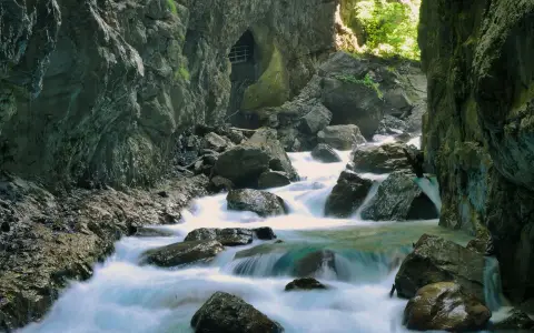 Symbolbild: Serene mountain stream cascading through mossy rocks in a tranquil gorge bathed in sunlight.