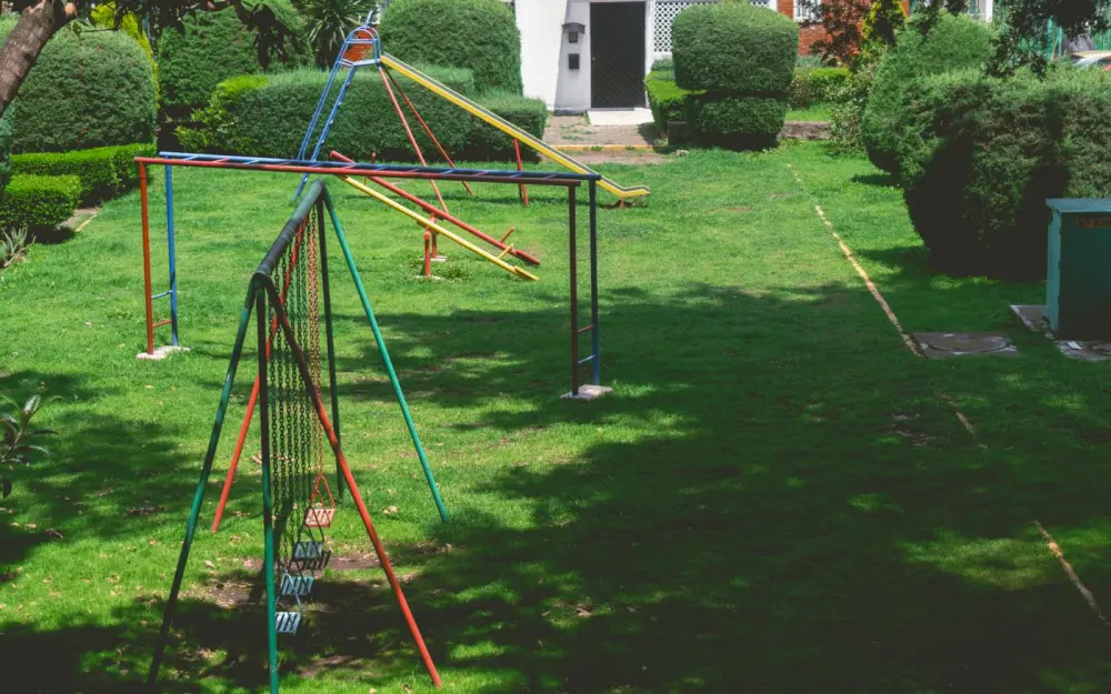 Symbolbild: Vibrant outdoor playground with swings and slides in a lush green park setting under a bright sky.