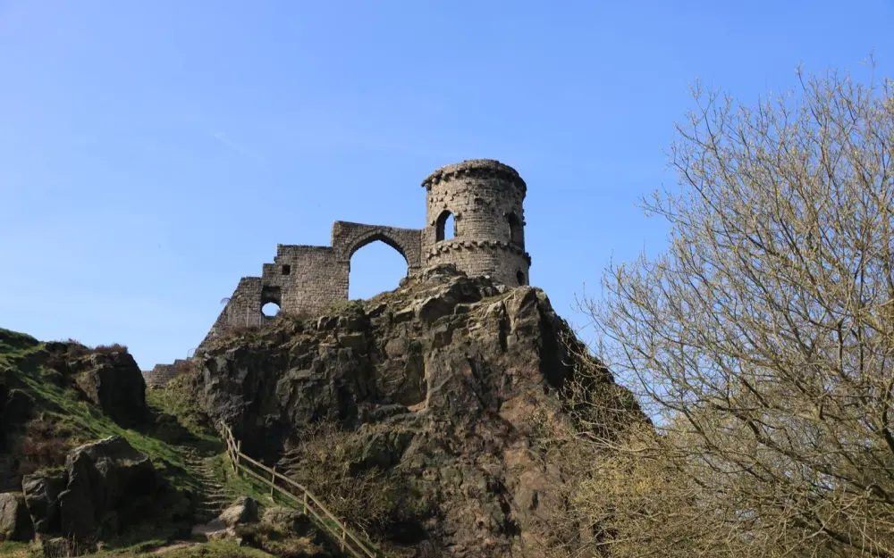 Symbolbild: Dramatic view of old castle remains atop a rocky hill in spring, captured under a clear blue sky.