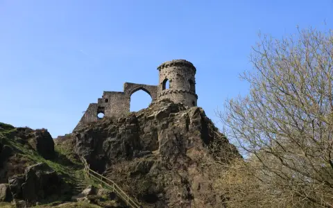 Symbolbild: Dramatic view of old castle remains atop a rocky hill in spring, captured under a clear blue sky.