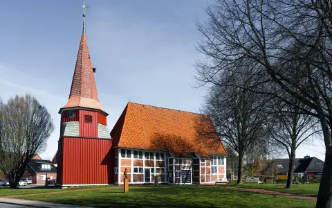 Symbolbild: A traditional red church with a pointed tower in Grünendeich, Niedersachsen, Germany, during spring.