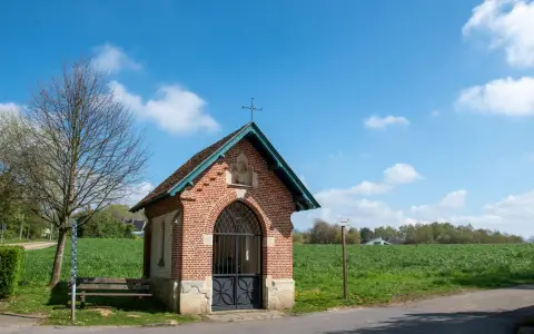 Symbolbild: A quaint brick chapel stands in Beersel, Belgium under a bright blue sky, surrounded by lush greenery.