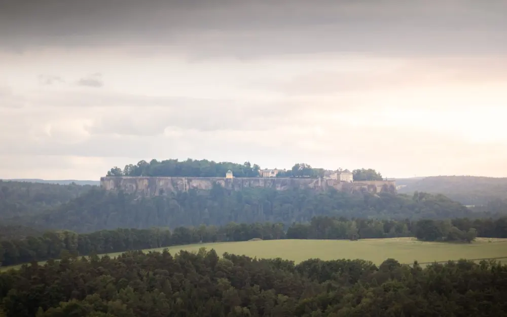 Symbolbild: Aerial shot of Festung Königstein in Saxony, surrounded by lush greenery and cloudy skies.