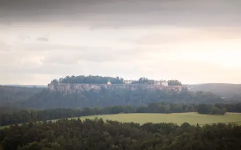 Symbolbild: Aerial shot of Festung Königstein in Saxony, surrounded by lush greenery and cloudy skies.