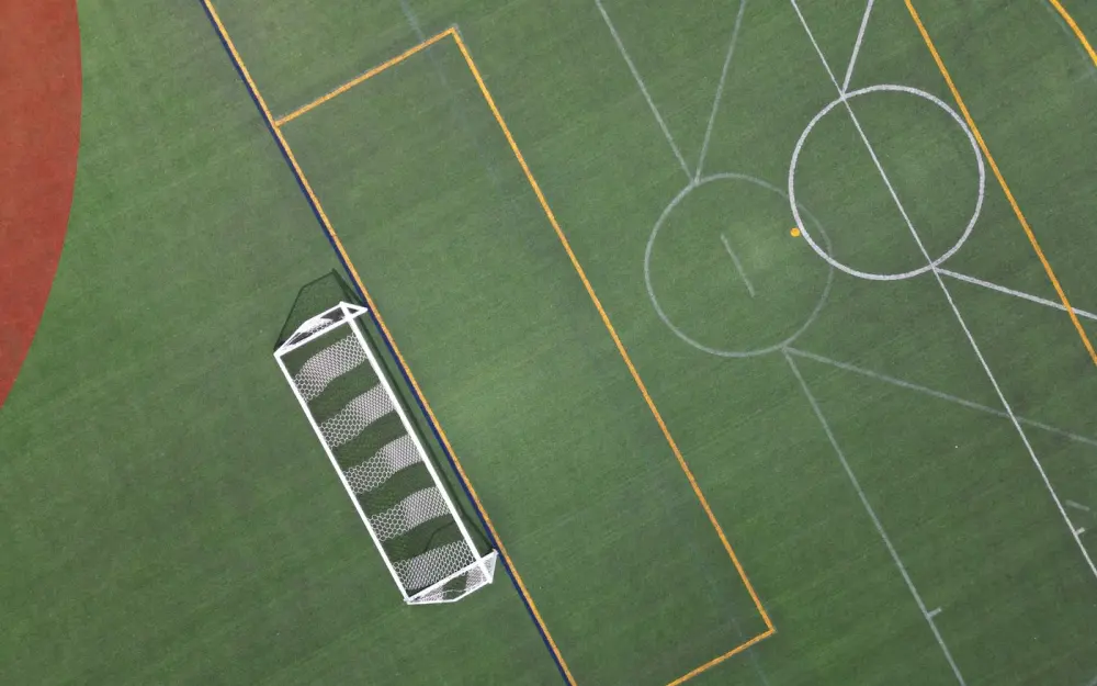Symbolbild: Top-down view of a vibrant, empty soccer field highlighting the goal net and pitch lines.