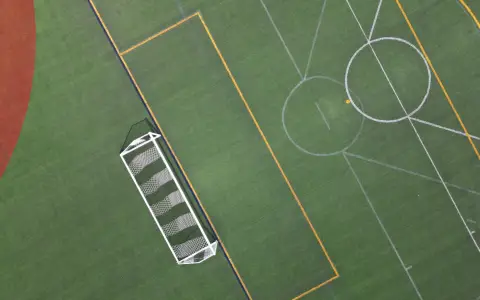 Symbolbild: Top-down view of a vibrant, empty soccer field highlighting the goal net and pitch lines.