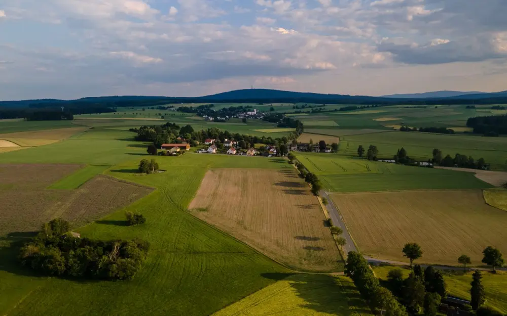 Symbolbild: Aerial shot of a picturesque rural landscape in Rehau, Germany, showcasing lush fields and a small village.