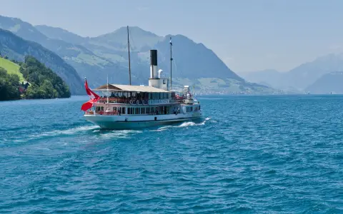Symbolbild: A historic steamboat navigates the blue waters of Lake Lucerne surrounded by majestic Swiss Alps under a clear sky.