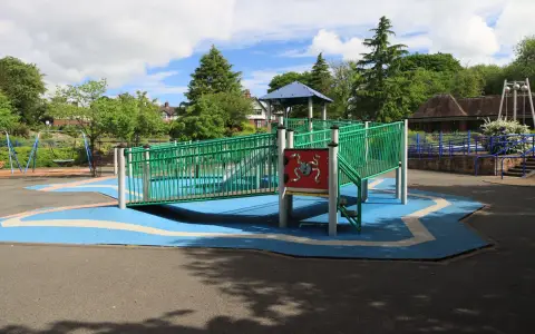 Symbolbild: A colorful playground with slides and swings in a sunlit park surrounded by greenery.