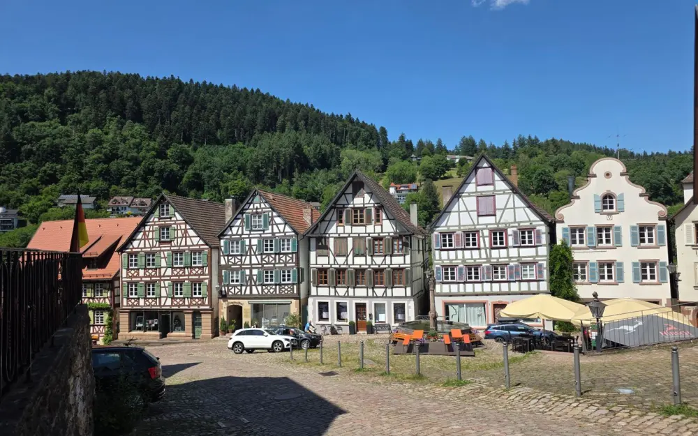 Symbolbild: Charming half-timbered houses in Schiltach, Germany under a clear blue sky, with scenic forest backdrop.