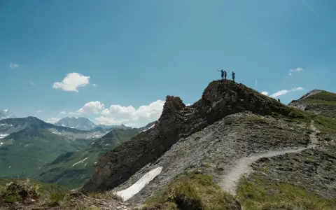 Symbolbild: Hikers stand on an Alpine ridge under a clear blue sky, showcasing natural beauty and adventure.