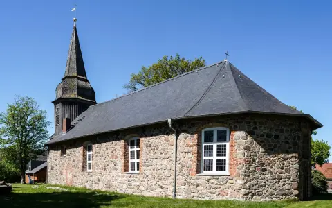 Symbolbild: Charming old stone church with steeple in Neu Wulmstorf, Germany, under blue sky.