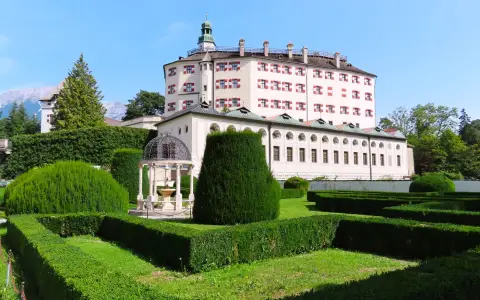 Symbolbild: Stunning view of Ambras Castle surrounded by meticulously maintained gardens under a clear blue sky.