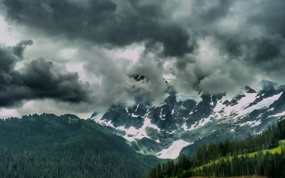 Symbolbild: A stunning view of a snow-capped mountain range surrounded by dark, dramatic clouds.