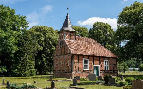 Symbolbild: Charming 18th-century brick and timber church in Greven, surrounded by lush greenery and gravestones.