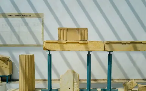 Symbolbild: Ancient Greek architectural fragments displayed in a museum with shadows.
