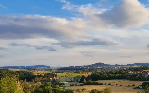 Symbolbild: A serene rural landscape in Fuldabrück, Germany featuring lush fields and a distant bridge under a blue sky.
