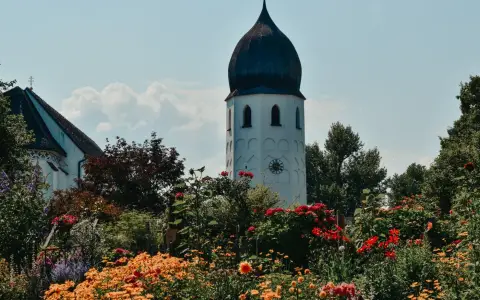 Symbolbild: Beautiful church tower surrounded by vibrant flowers under a clear sky at Chiemsee, Germany.