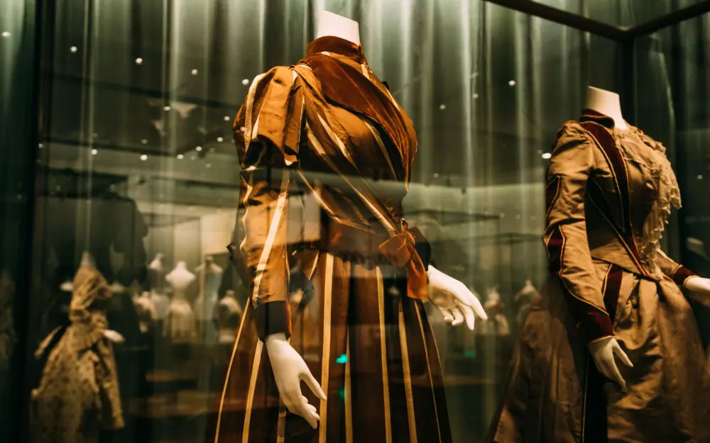 Symbolbild: Through glass view of bright ornamental aged style feminine dresses on mannequins in museum