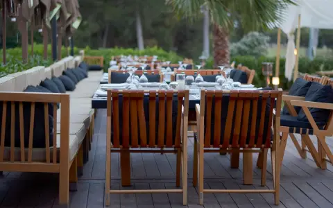 Symbolbild: Elegant resort patio with wooden furniture set for outdoor dining in a serene environment.