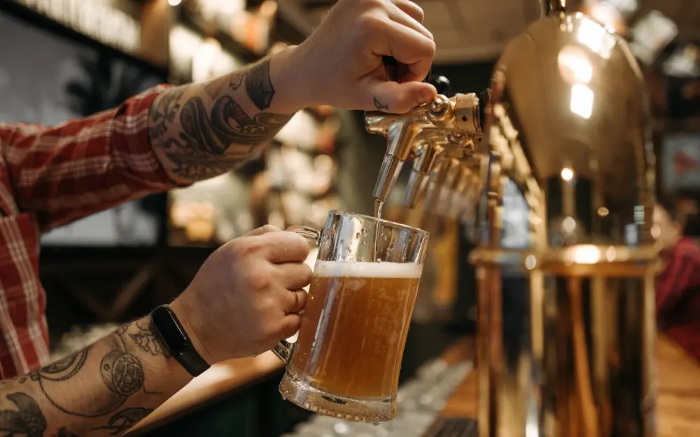 Symbolbild: Close-up of a bartender pouring a cold draft beer into a glass mug at a bar.