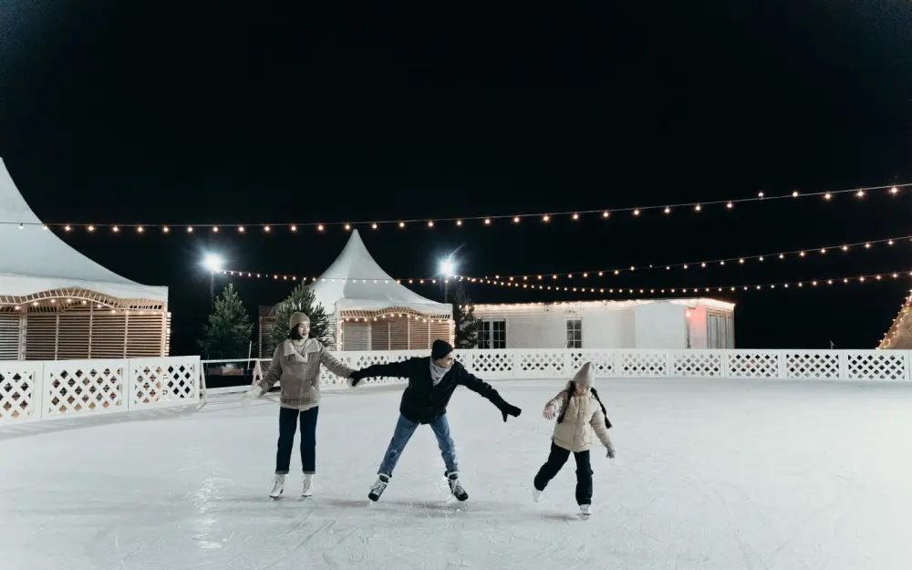 Symbolbild: A family enjoying ice skating together on an outdoor rink at night under festive string lights.