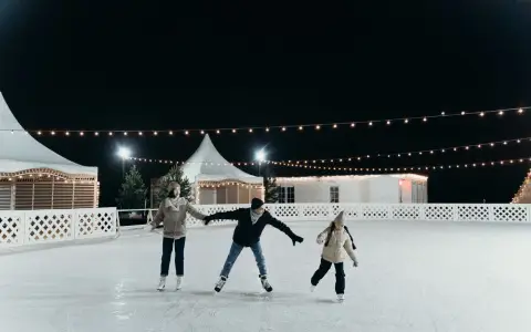 Symbolbild: A family enjoying ice skating together on an outdoor rink at night under festive string lights.