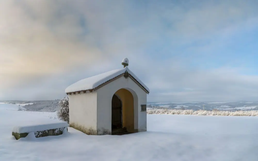 Symbolbild: A lone chapel in a snowy field, illustrating winter's peaceful beauty.