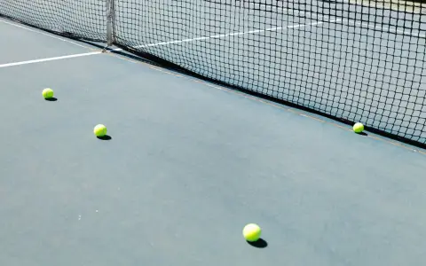 Symbolbild: A tennis court featuring a net and several tennis balls lying on the ground, well-lit by sunlight.