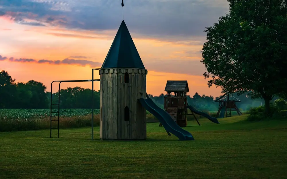 Symbolbild: Charming rural playground with slides and towers under a vibrant sunset sky.