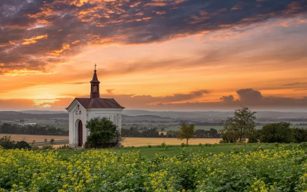 Symbolbild: Charming chapel surrounded by fields under a vibrant sunset sky.