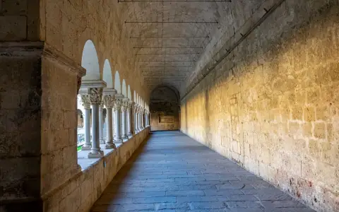 Symbolbild: A serene stone corridor of a historic monastery in Sant Cugat, bathed in natural light.