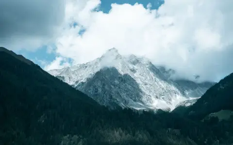 Symbolbild: Captivating view of majestic mountain peaks surrounded by lush forest and cloudy sky.
