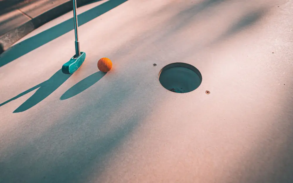 Symbolbild: Close-up shot of a mini golf putter and ball near the hole on a sunny day.